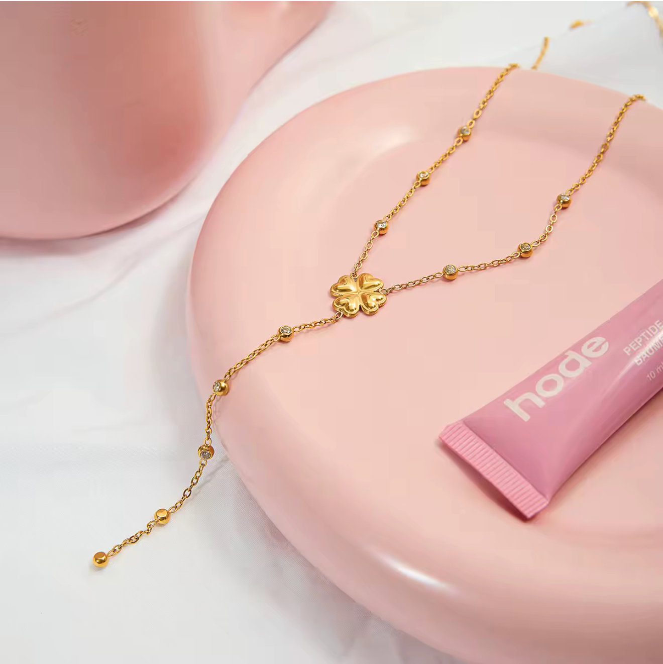 Gold necklace on a pink stand with a pink tube of lip balm, displayed on a smartphone screen.